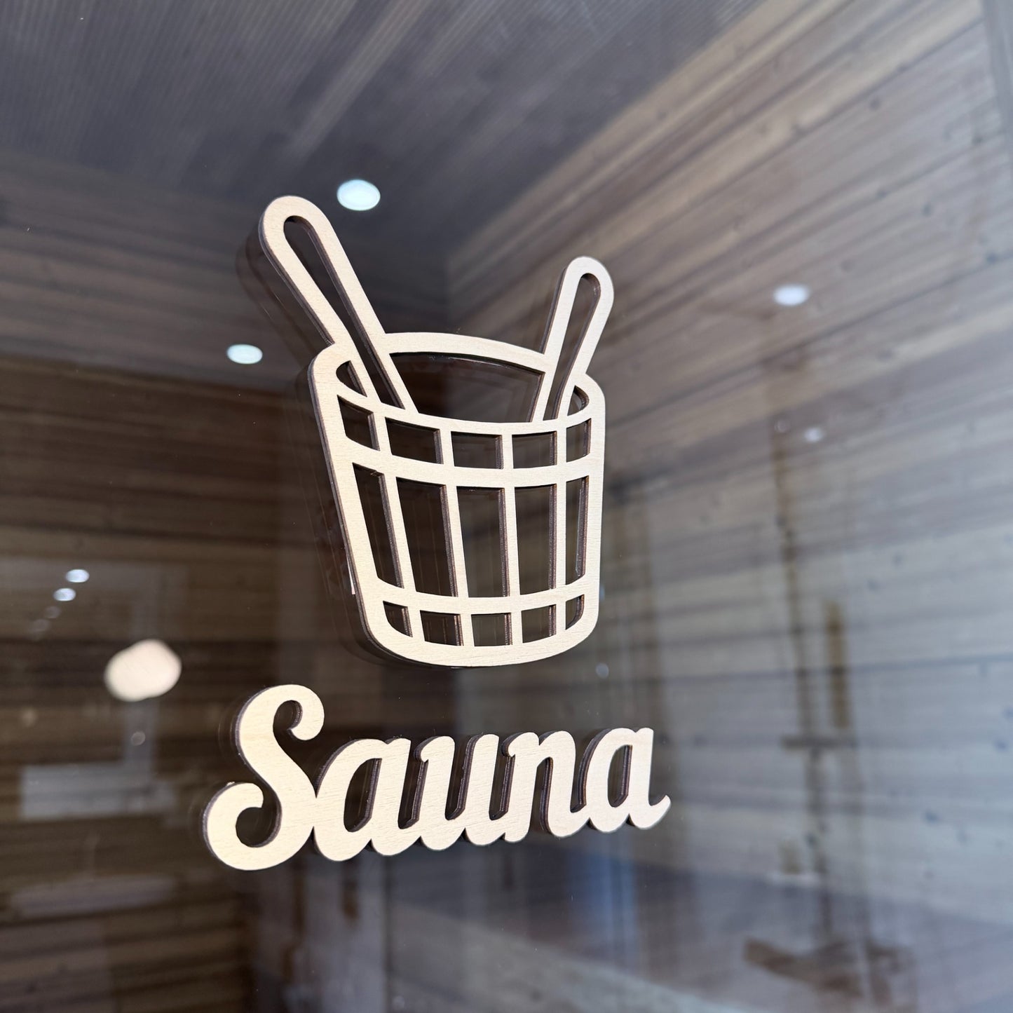 Puinen saunakiulu-kyltti saunan lasiovessa